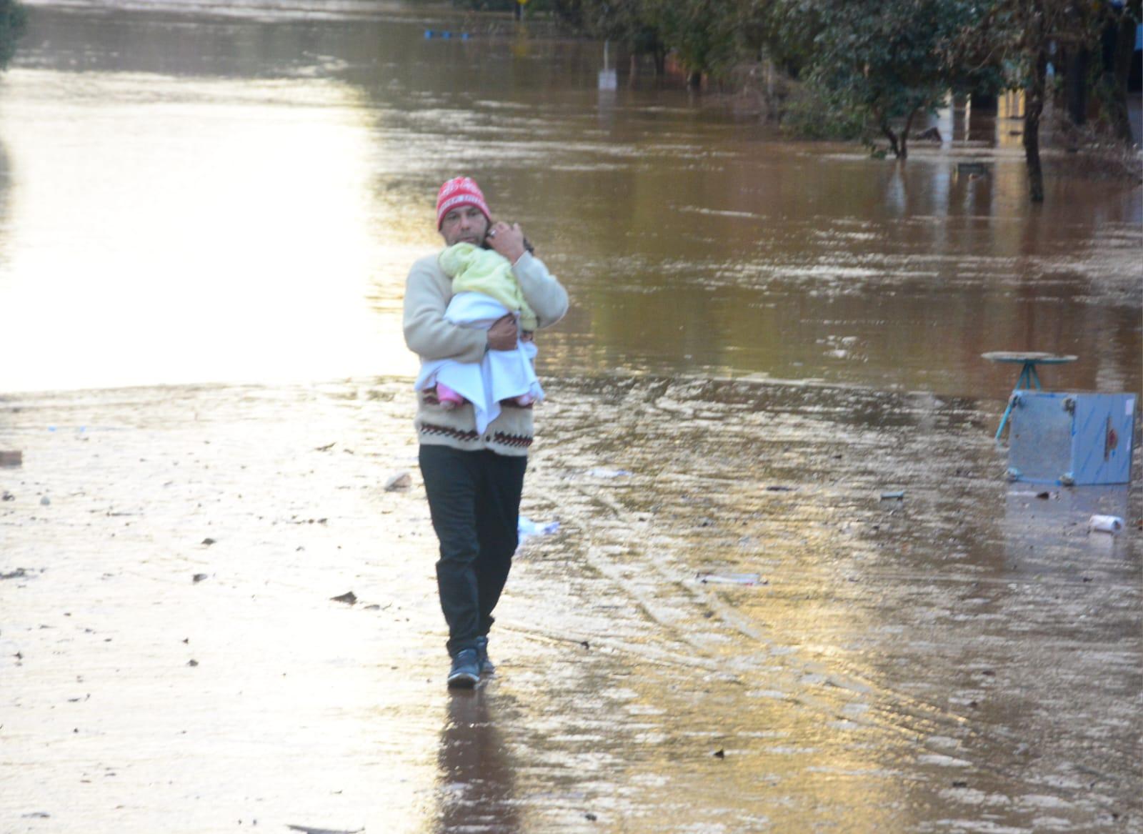 Beb&ecirc; sendo carregada pelo pai em meio a enchente em Estrela.